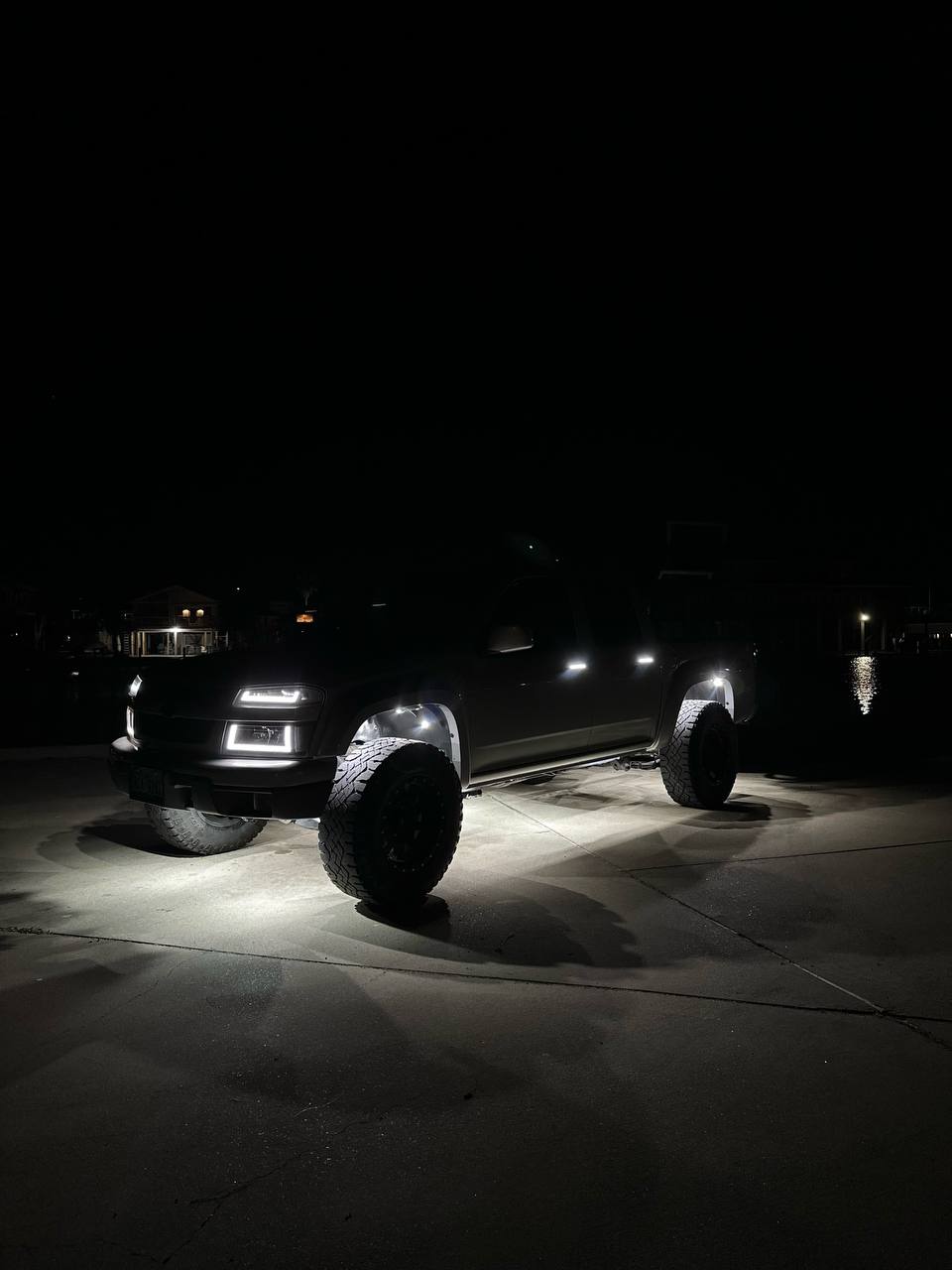 Pure White 9 LED rock lights lighting the concrete under a lifted pickup parked by the water at night