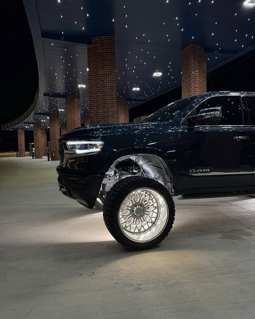 Pure White Ultimate Intensity wheel lights lit white on the front wheel of a lifted black 5th gen Ram under a canopy at night