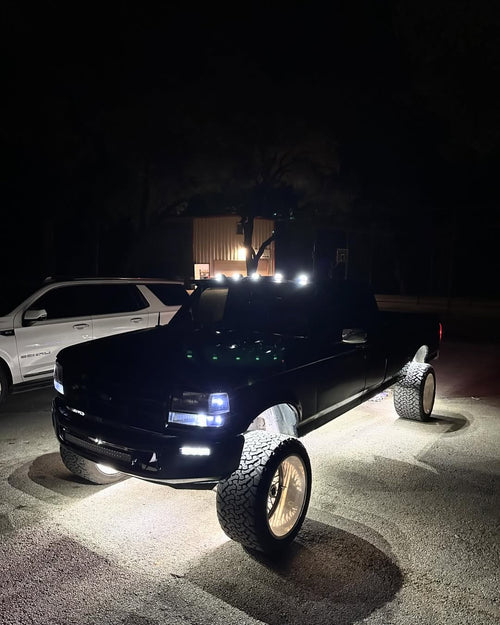 Pure White High Intensity wheel lights lit white under a black lifted pickup in a parking lot at night